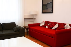 Una sala de estar con un sofá rojo, un sofá oscuro, una lámpara y un cuadro en la pared.