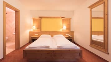 A double bed with wooden headboard and footboard, two bedside tables with lamps, a mirror on the wall, and a wooden wardrobe.