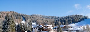 A snow-covered mountain village with traditional wooden houses, a ski lift, and a clear blue sky. - Berghotel Zum Zirm (Renon)