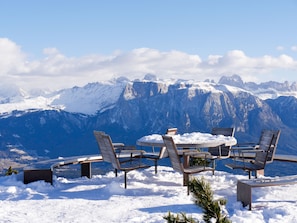 Un espacio al aire libre cubierto de nieve con una mesa y sillas, con vistas a un paisaje montañoso.