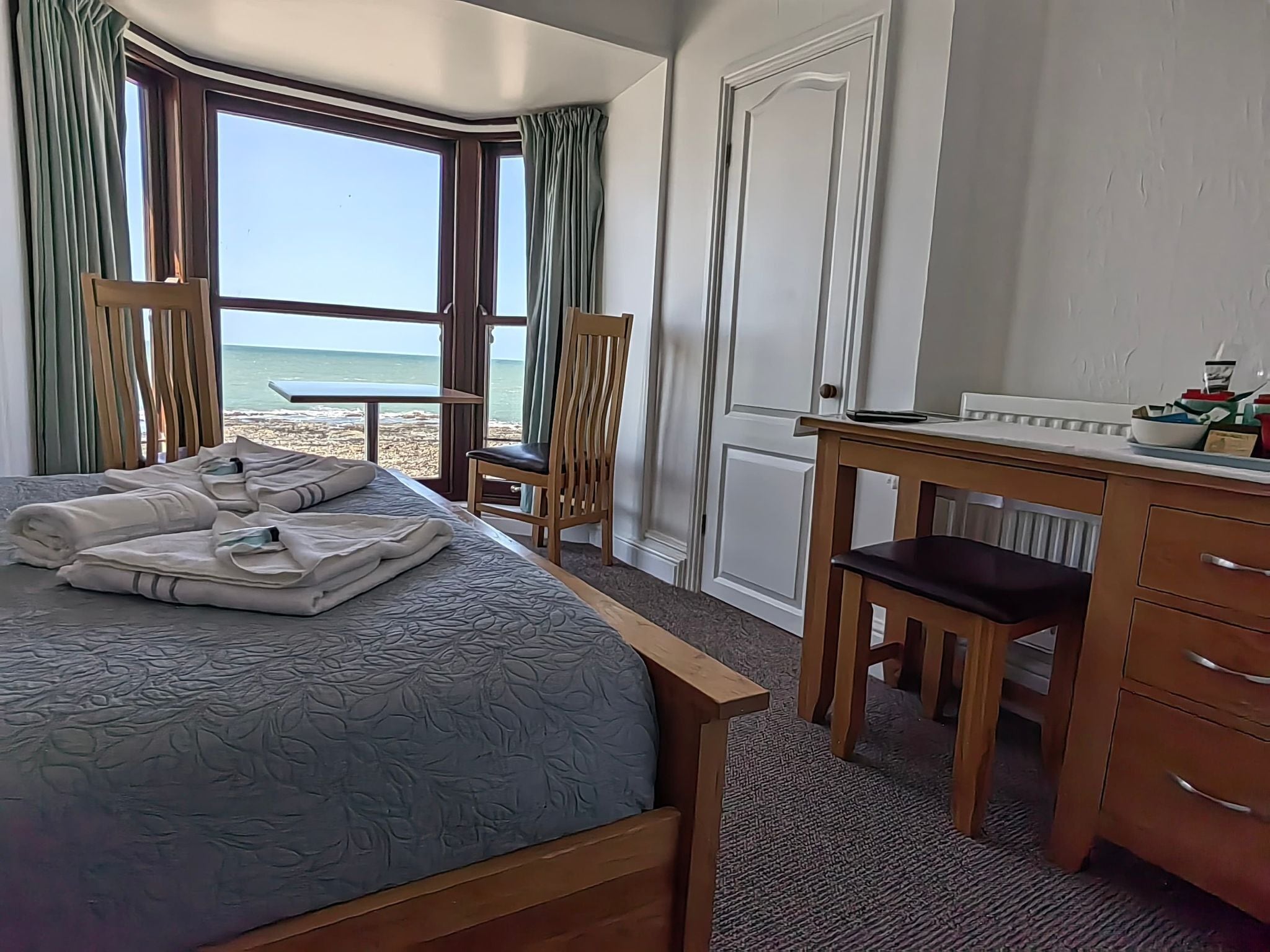 Een hotelkamer met een bed, een bureau, een stoel en uitzicht op het strand.