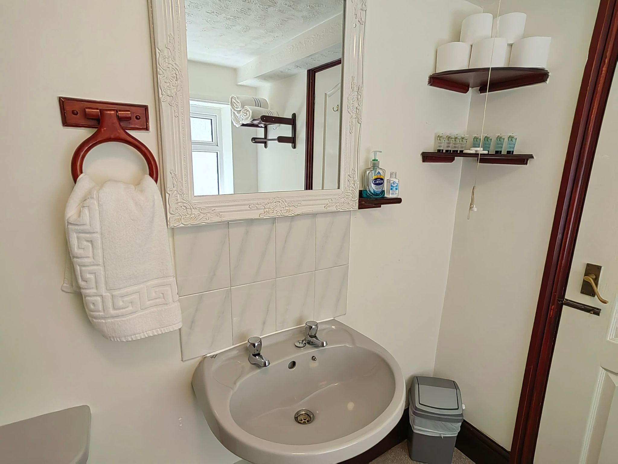 Un baño con lavamanos, espejo, toallero, inodoro y un cubo de basura.