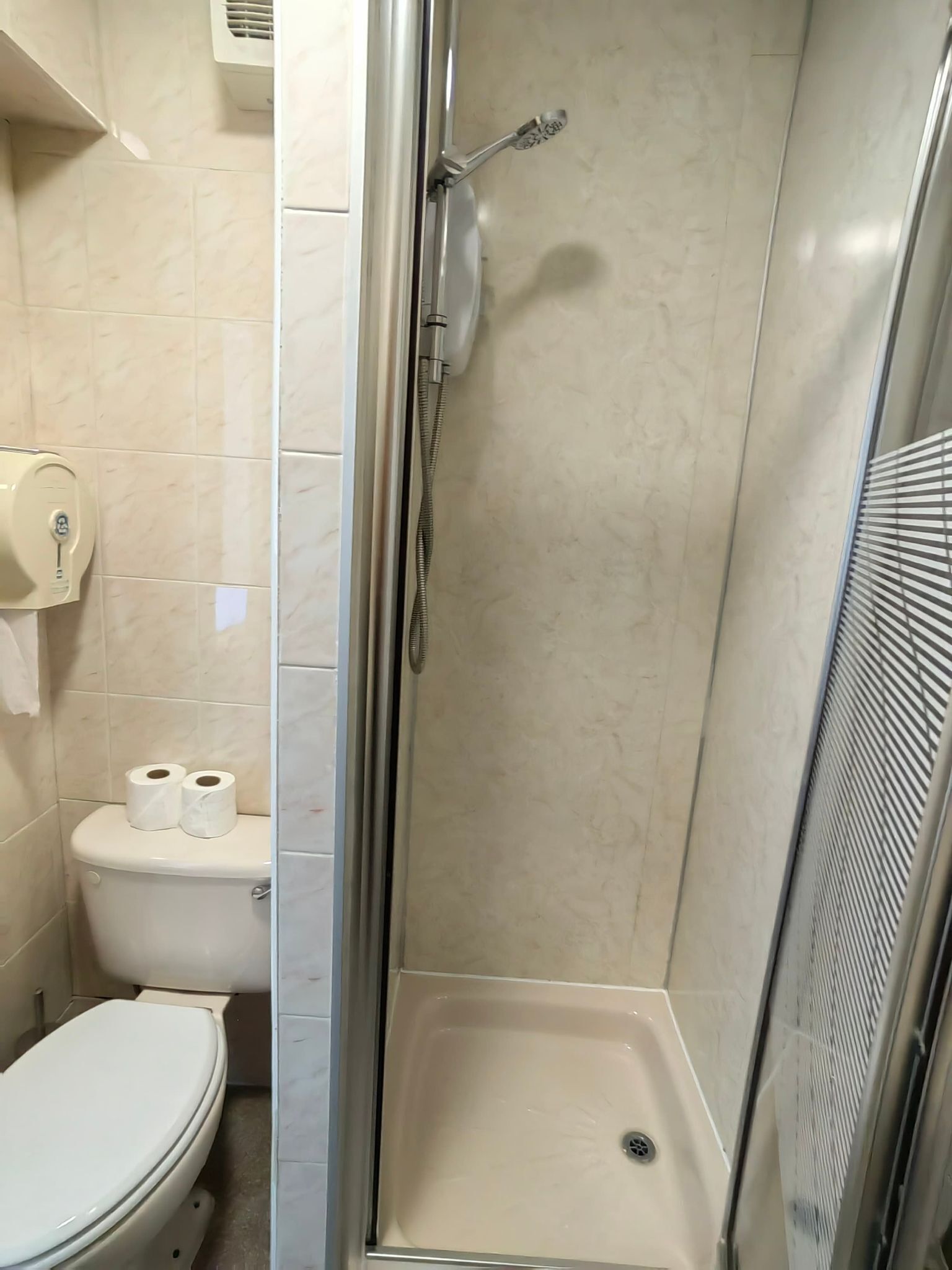 Ein kleines Badezimmer mit Toilette, Dusche und einem Handtrockner.