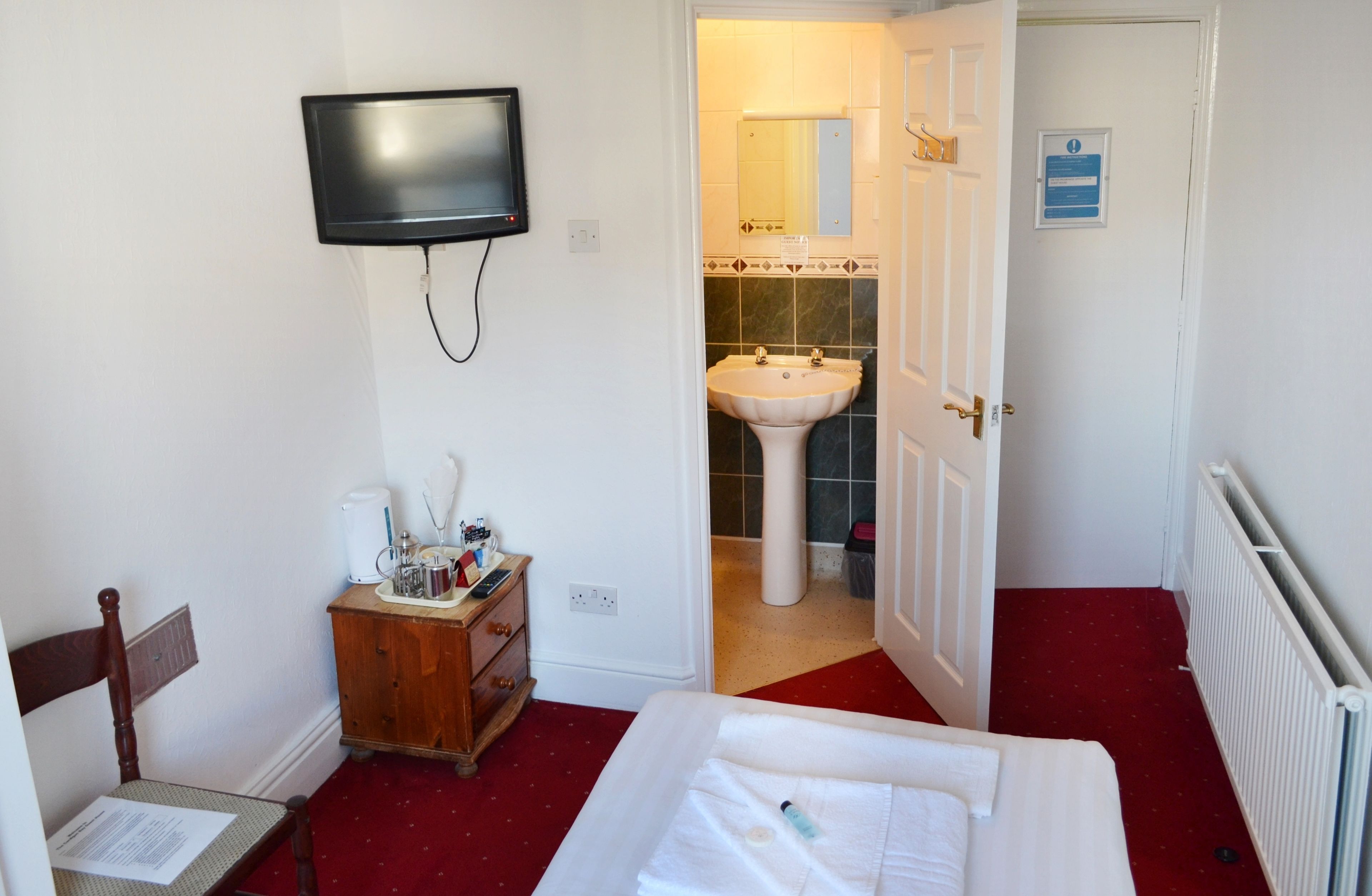 A hotel room with a bed, a wooden nightstand with toiletries, a television mounted on the wall, and a bathroom visible through an open door.