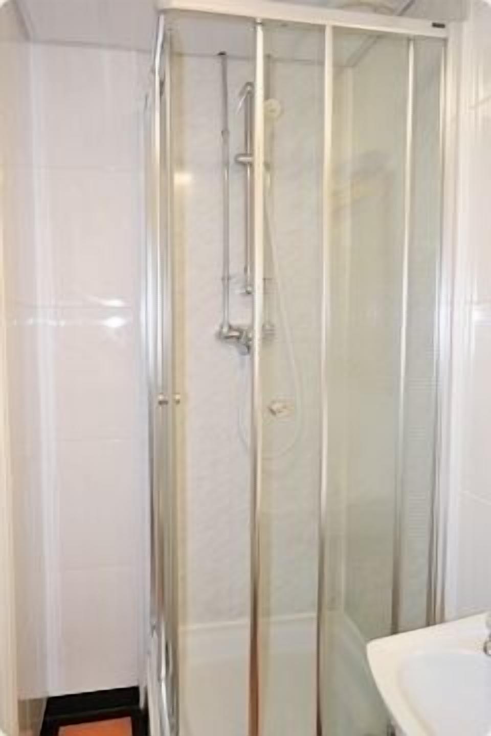 Ducha con mampara de vidrio, cabezal de ducha manual y grifo monomando.