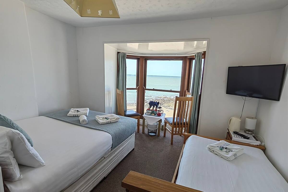 Ein Hotelzimmer mit zwei Betten, einem Fernseher, einem Tisch mit einem Stuhl und Blick auf den Strand.