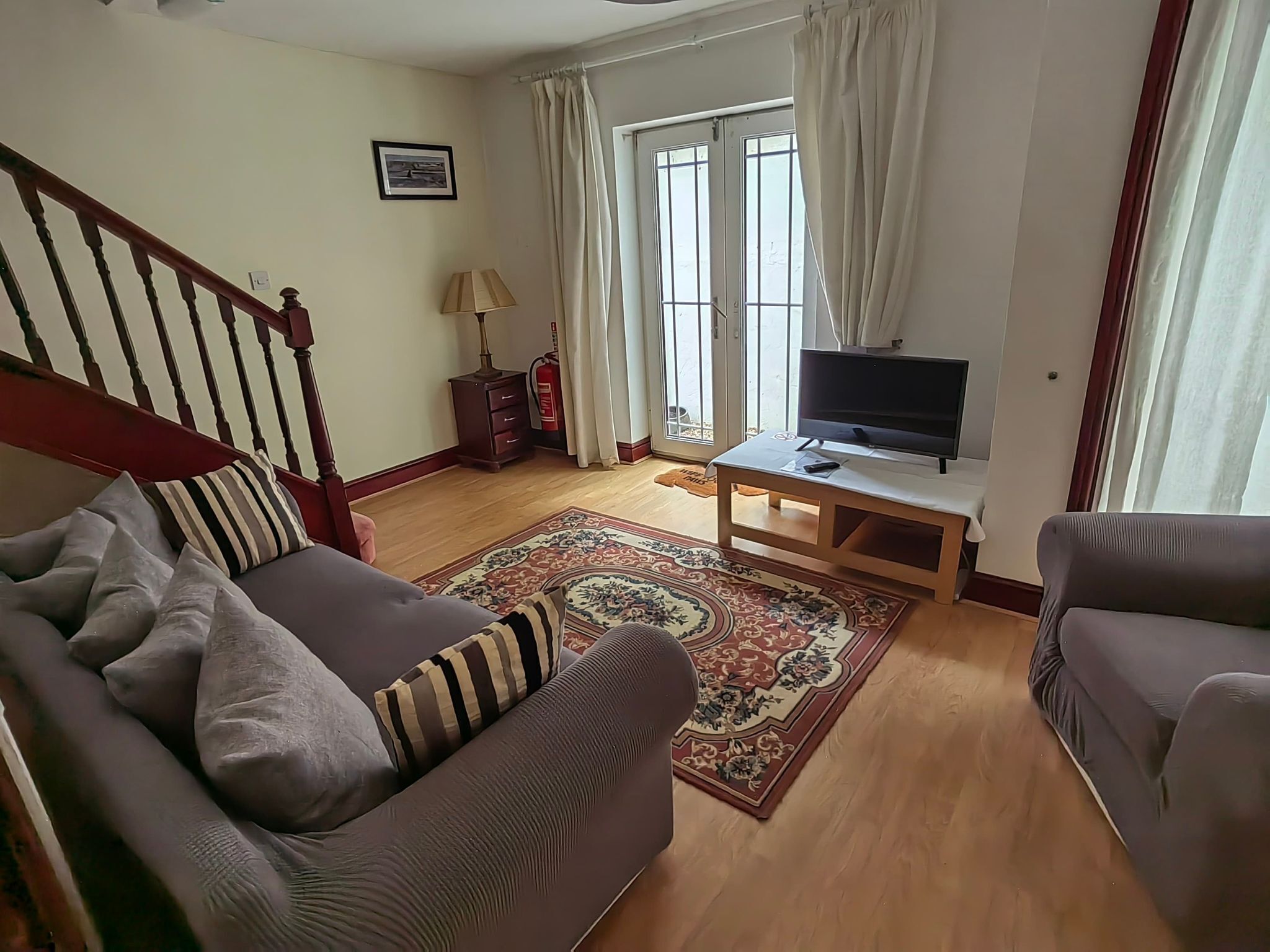 Una sala de estar con un sofá, un televisor sobre un mueble bajo, un tapete estampado y una escalera.