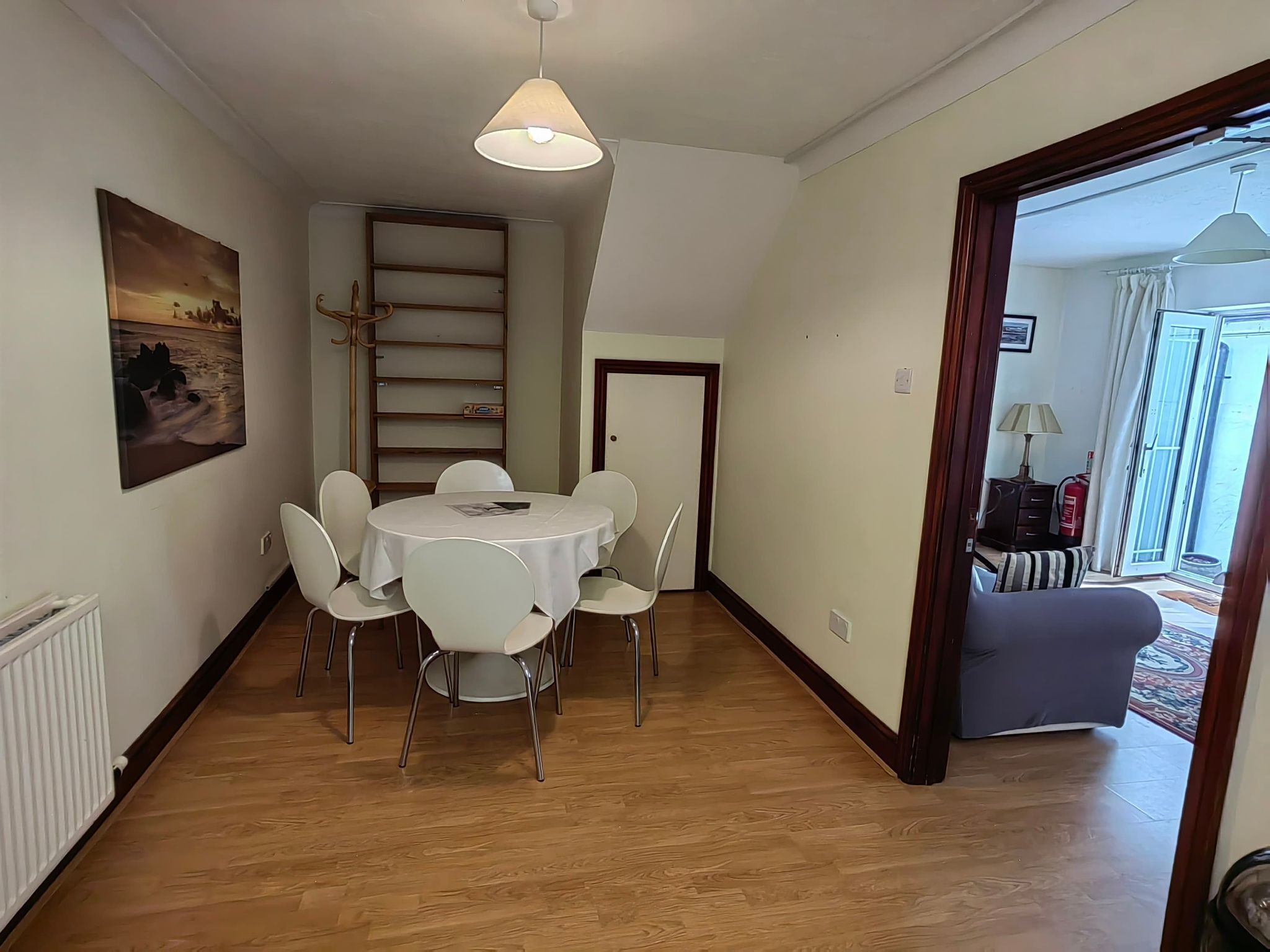 Un comedor con una mesa redonda y sillas, un lámpara colgante, una estantería y una puerta que da a otra habitación.