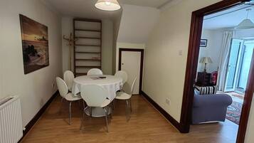 Un comedor con una mesa redonda y sillas, un lámpara colgante, una estantería y una puerta que da a otra habitación.