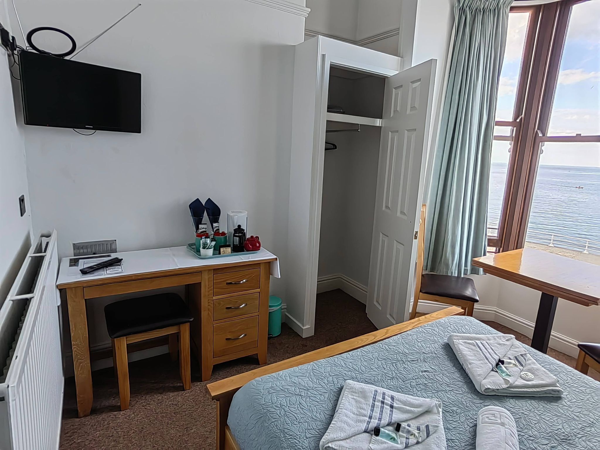 Una habitación de hotel con una cama, un escritorio con una silla, un televisor montado en la pared y vista al mar por la ventana.