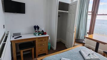 Una habitación de hotel con una cama, un escritorio con una silla, un televisor montado en la pared y vista al mar por la ventana.