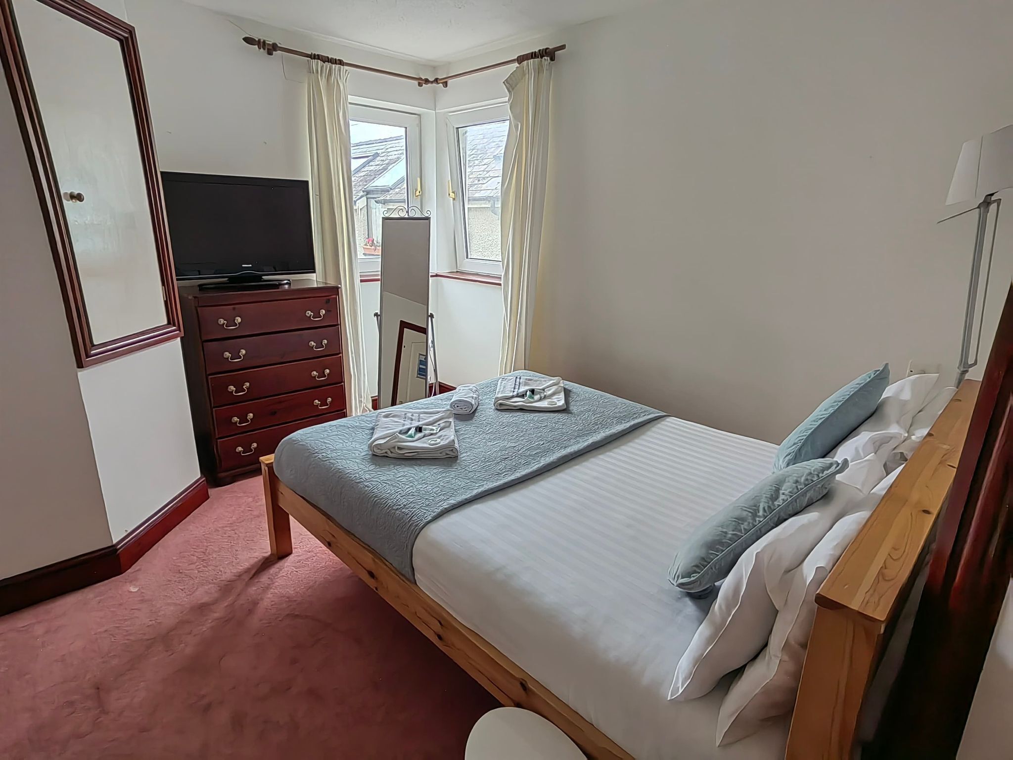 Un dormitorio con cama, cómoda, televisor y ventana con cortinas.