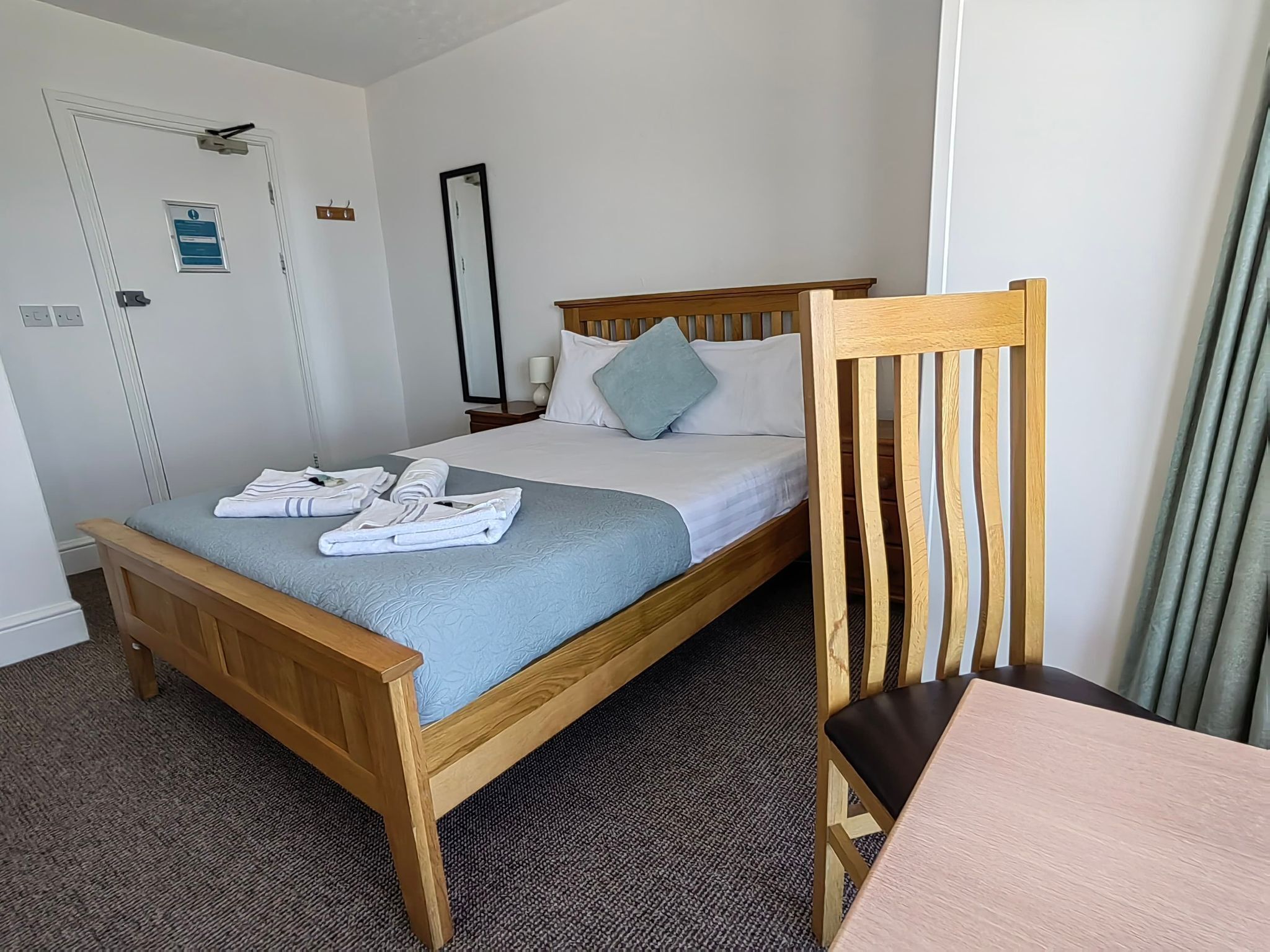 A hotel room with a wooden bed, a nightstand, a mirror, and a chair.
