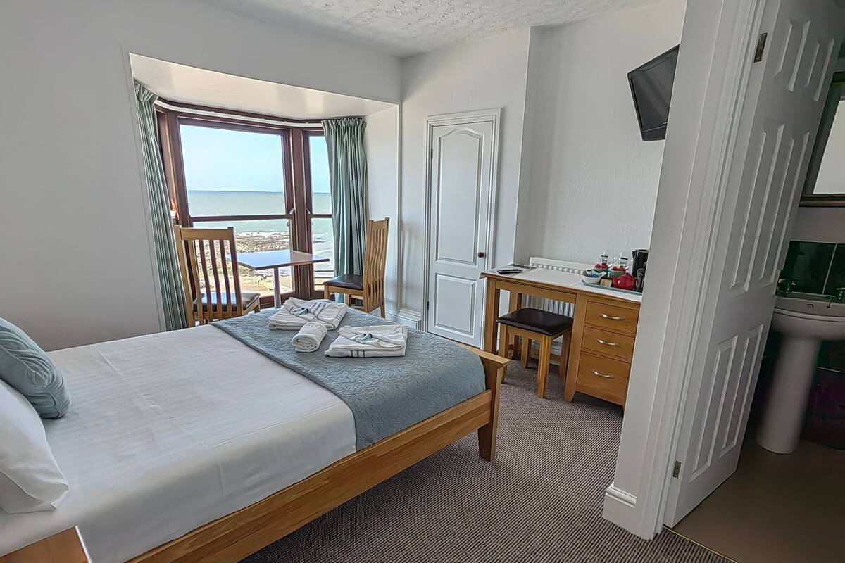 Ein Schlafzimmer mit Bett, Schreibtisch, Stuhl, Fernseher und Meerblick.