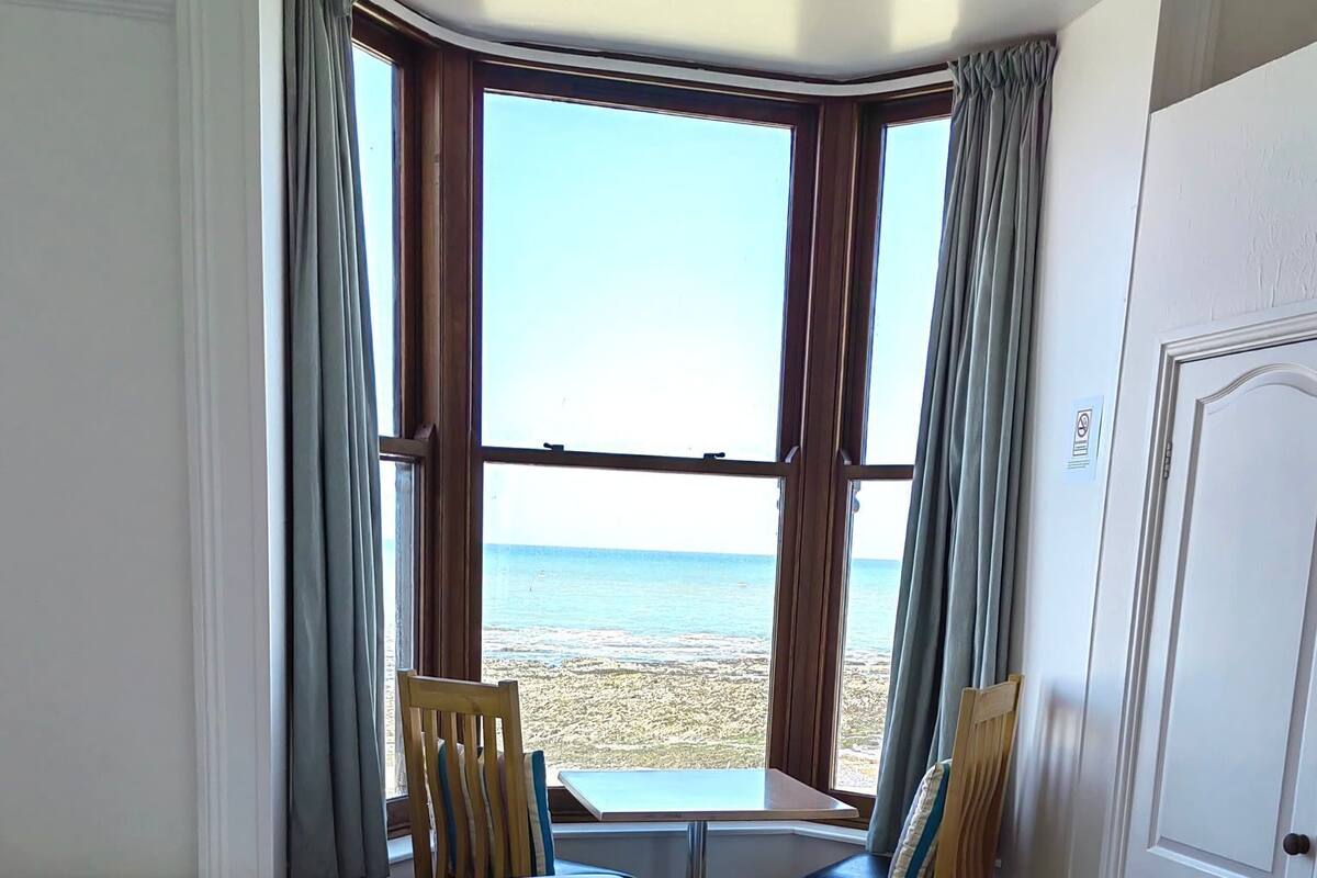 Ein Hotelzimmer mit zwei Betten, einem kleinen Tisch, einem Stuhl und Blick auf den Strand.