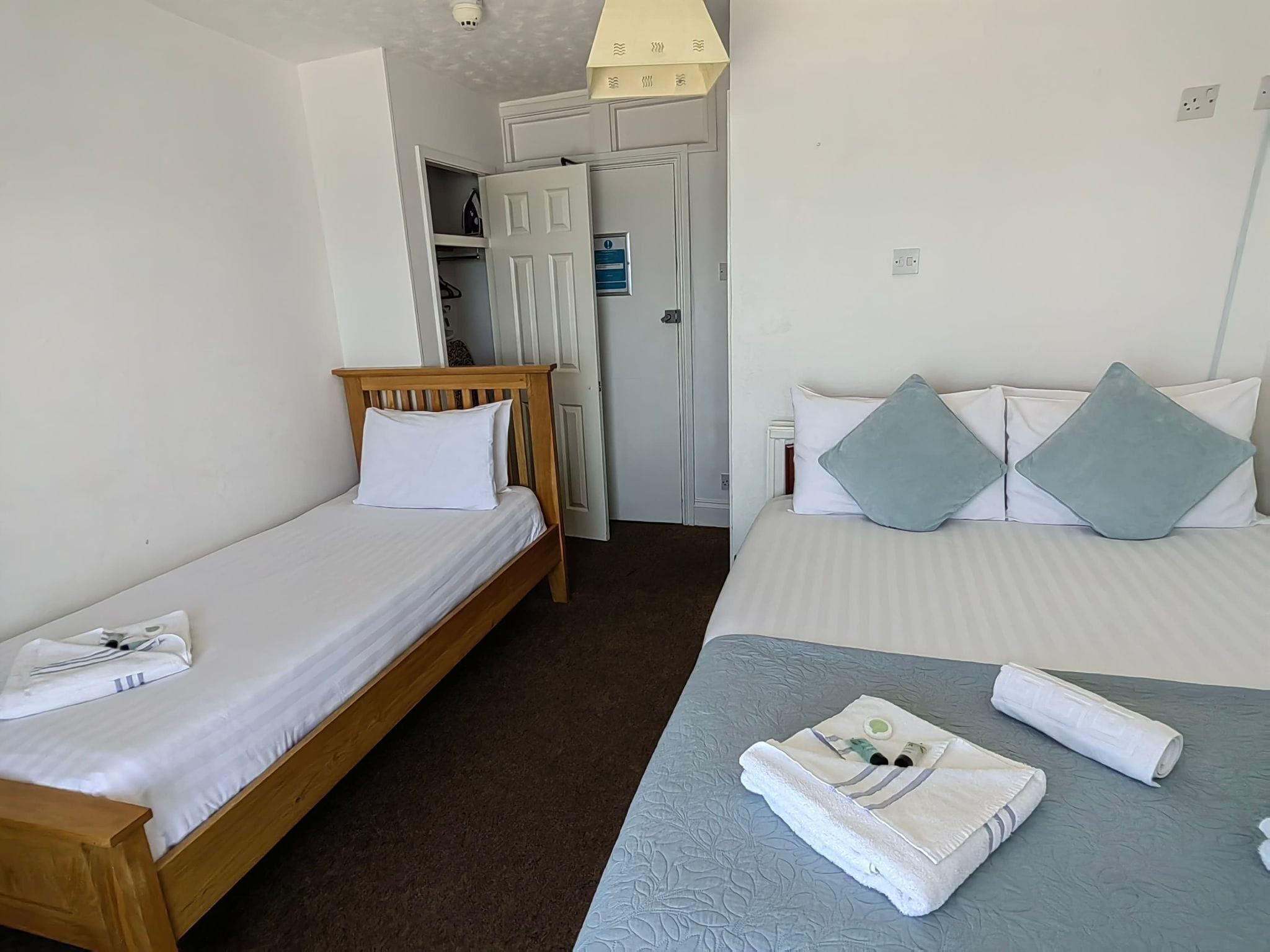 Een hotelkamer met twee enkele bedden, een houten hoofdbord, een blauw geweven sprei en een witte handdoek op de vloer.