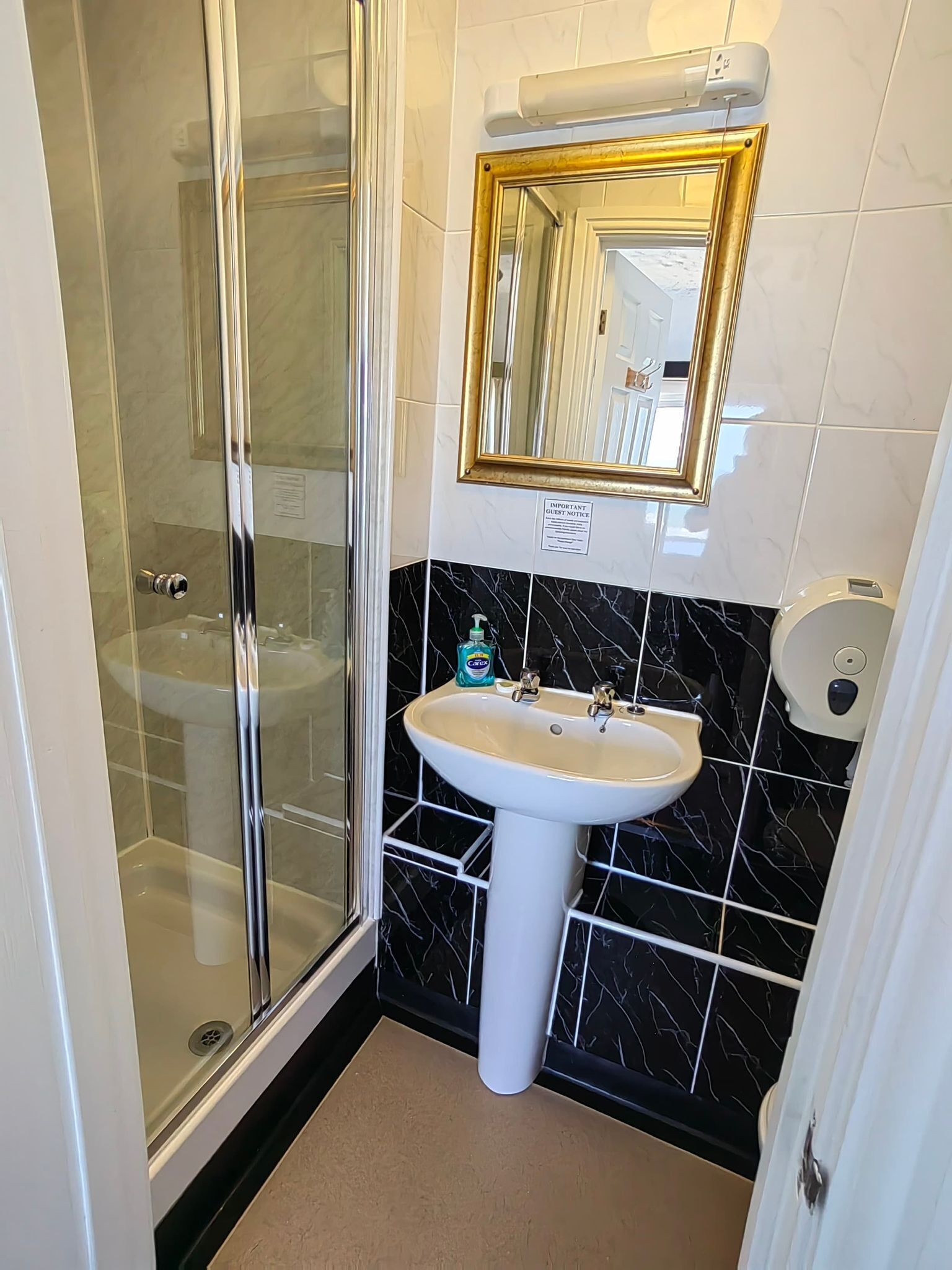 A bathroom with a glass-enclosed shower, a pedestal sink, and a wall-mounted mirror with a gold frame.