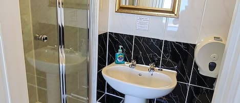 A bathroom with a glass-enclosed shower, a pedestal sink, and a wall-mounted mirror with a gold frame.