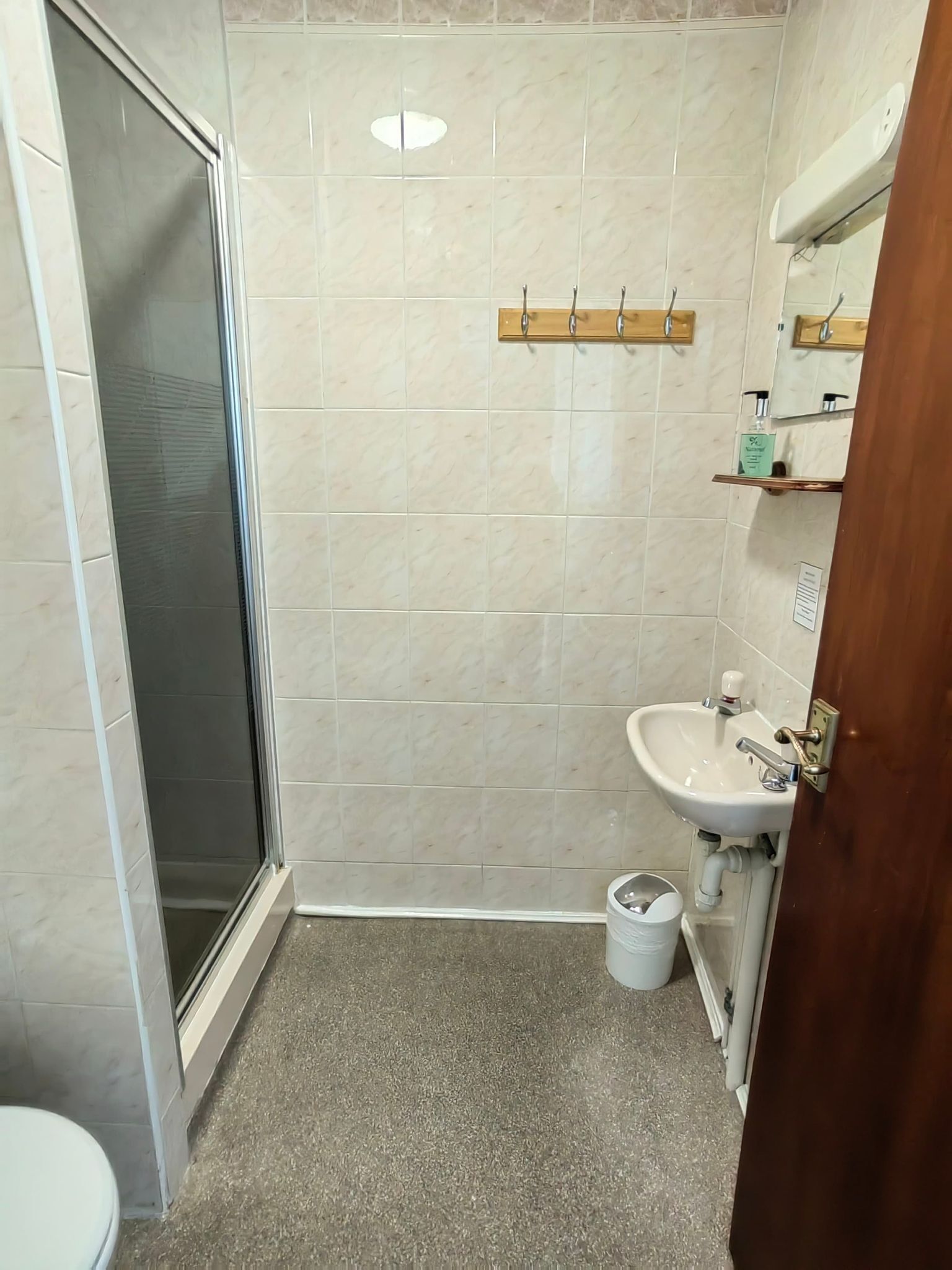 A bathroom with a shower, toilet, sink, and a small trash bin.