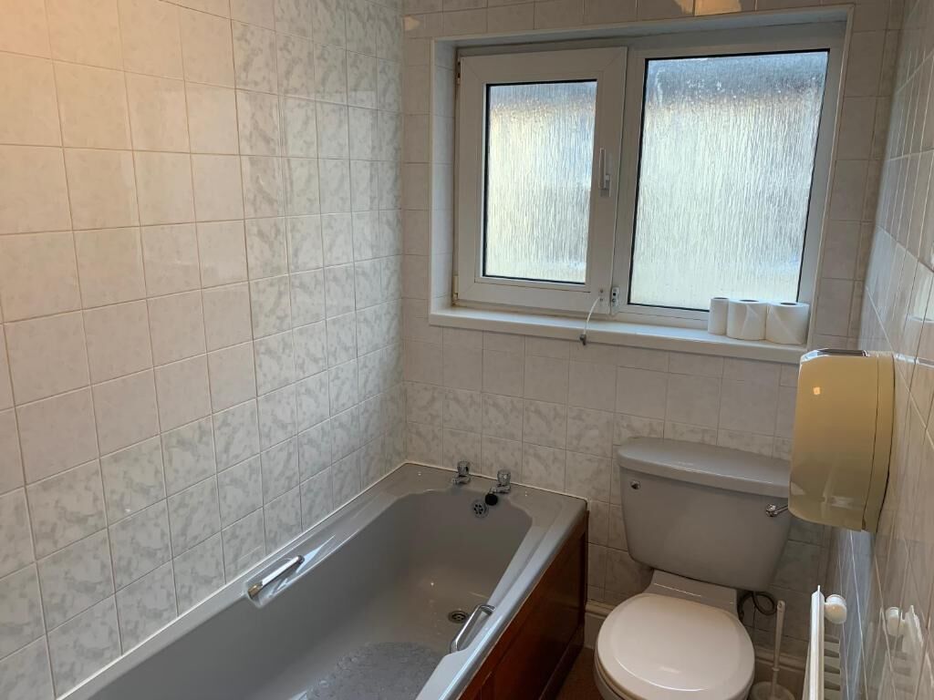 Un baño con bañera, inodoro y una ventana sobre el inodoro.