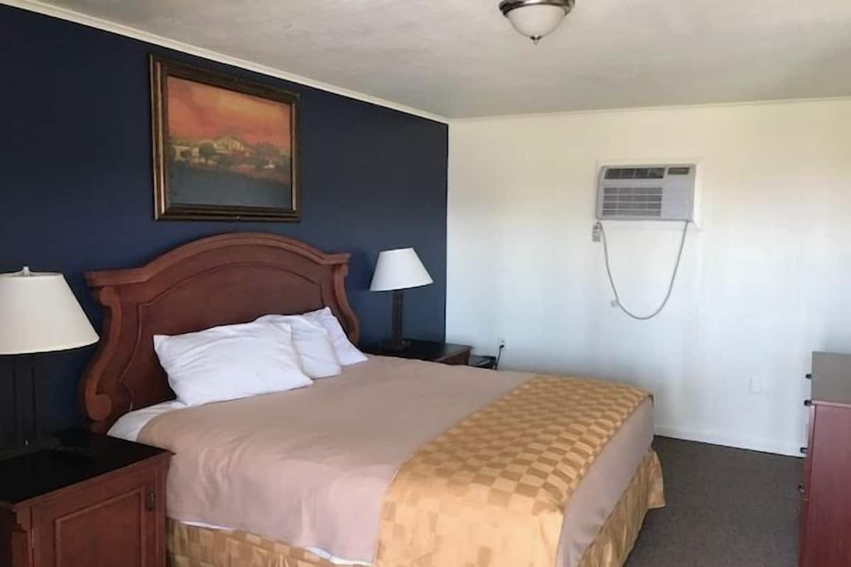 Une chambre à coucher avec un lit, deux tables de chevet avec des lampes, un climatiseur fixé au mur et un tableau au-dessus du lit.