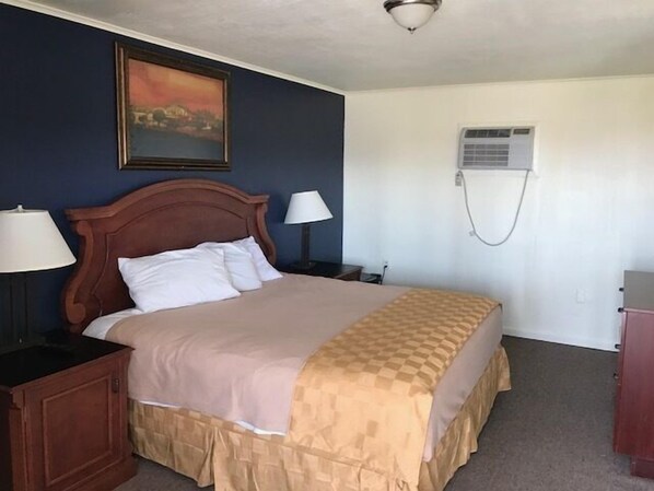 Un dormitorio con una cama, dos mesitas de noche con lámparas, un aire acondicionado instalado en la pared y un cuadro sobre la cama.