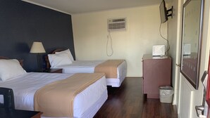 A hotel room with two beds, a desk, a lamp, a small cabinet, a trash bin, and a wall-mounted air conditioning unit. - Sunset Inn (Atlantic City)