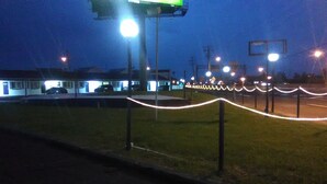 A parking lot with a green sign, a building with a white facade, and a grassy area with a white rope barrier. - Sunset Inn (Atlantic City)
