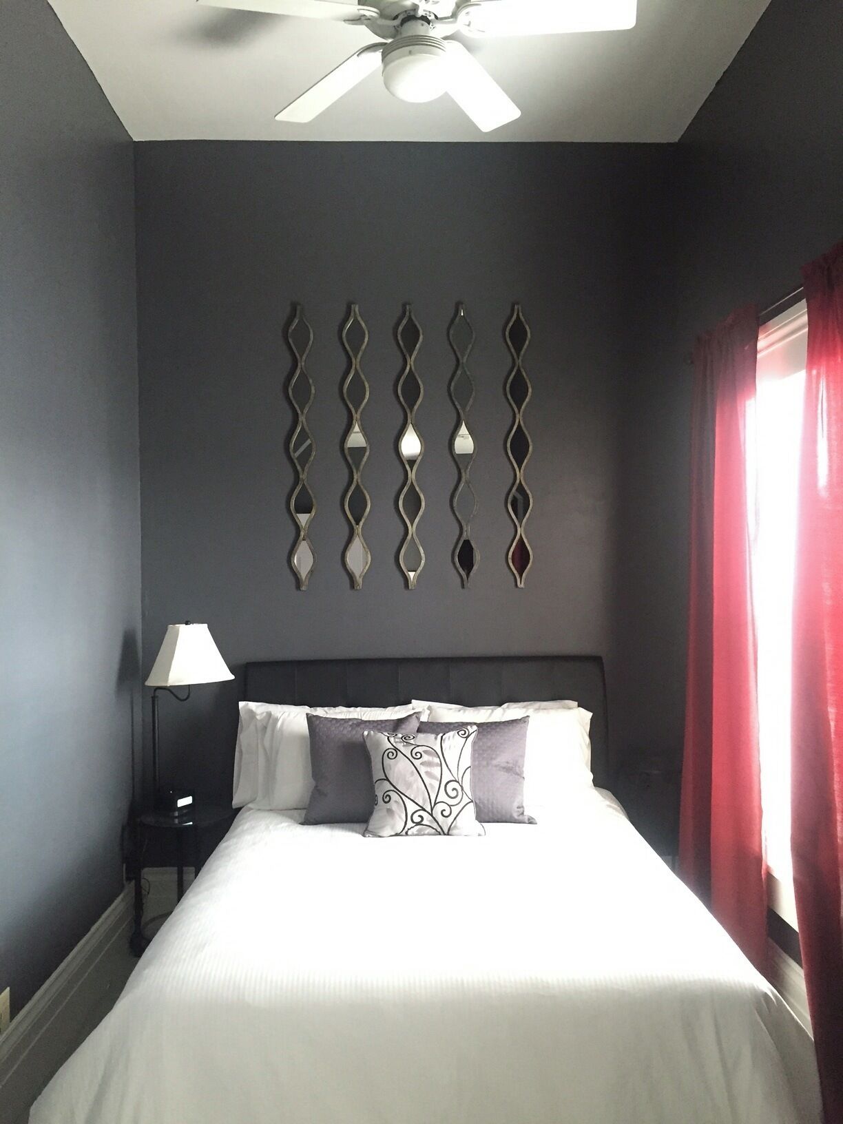 A bedroom with a bed, a nightstand, a lamp, a ceiling fan, and a decorative wall piece.