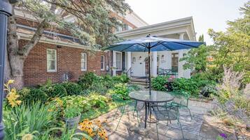 Un patio con mesa y sillas, rodeado por un jardín con diversas plantas y flores.