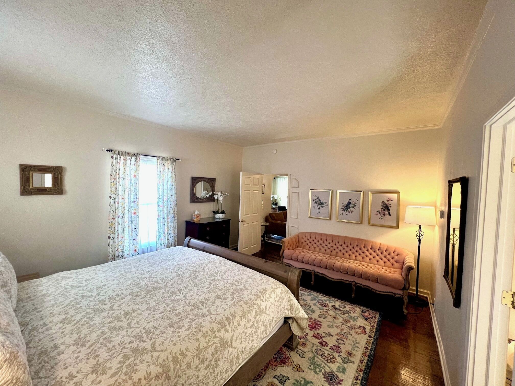 A bedroom with a large bed, a sofa, a dresser, and a mirror.