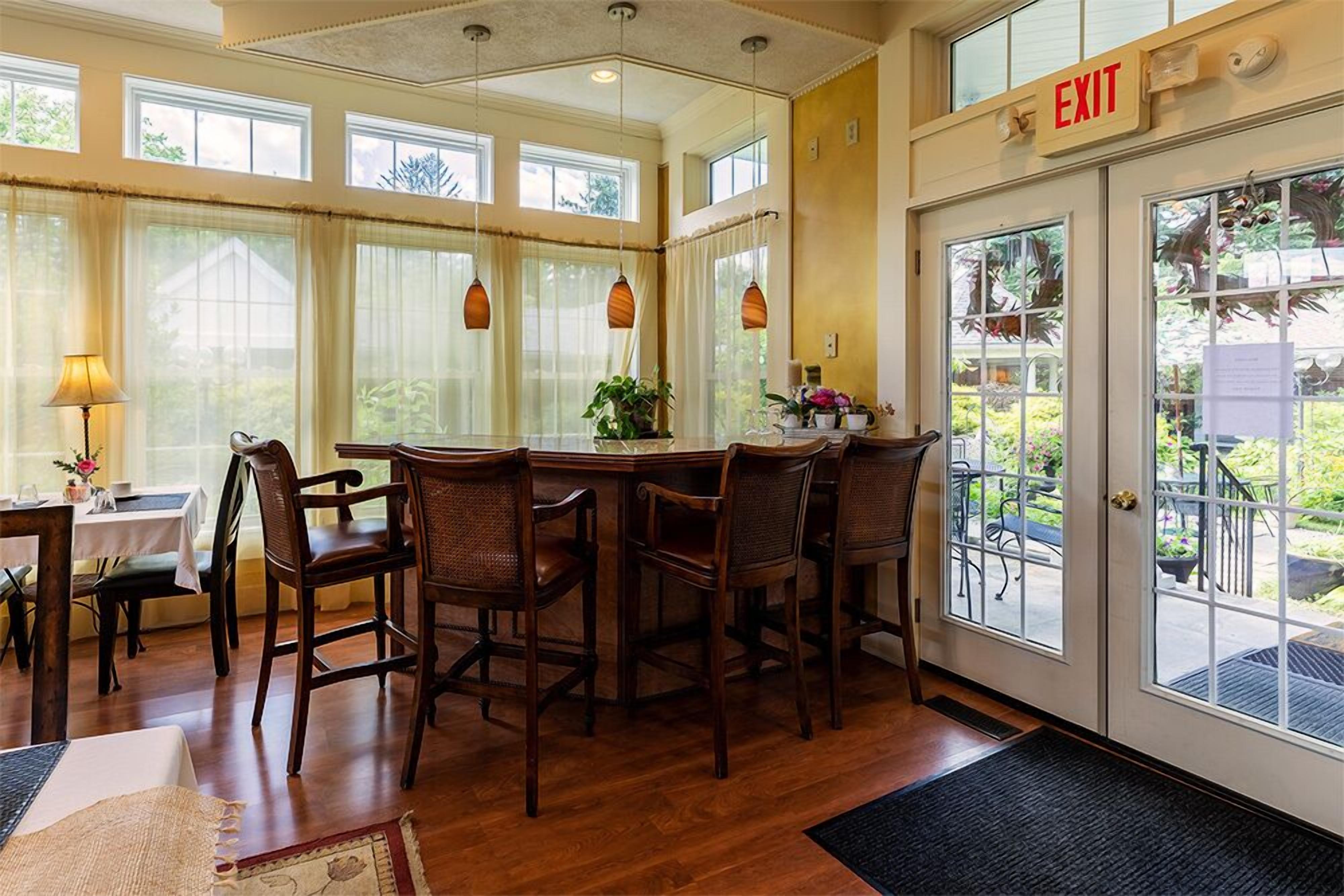 A dining area with a wooden table and chairs, a window with curtains, and an exit sign.