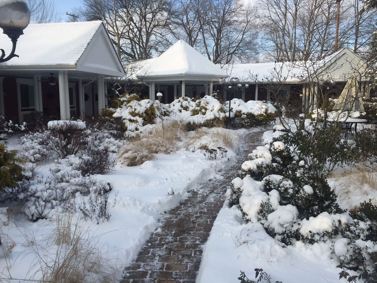 A snow-covered pathway leading to a house with a covered porch and a snow-covered roof.
