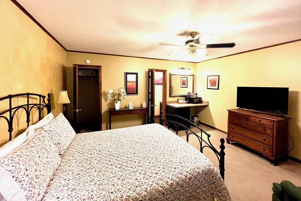 A hotel room with a bed, a dresser, a television, a desk with a lamp, and a ceiling fan.