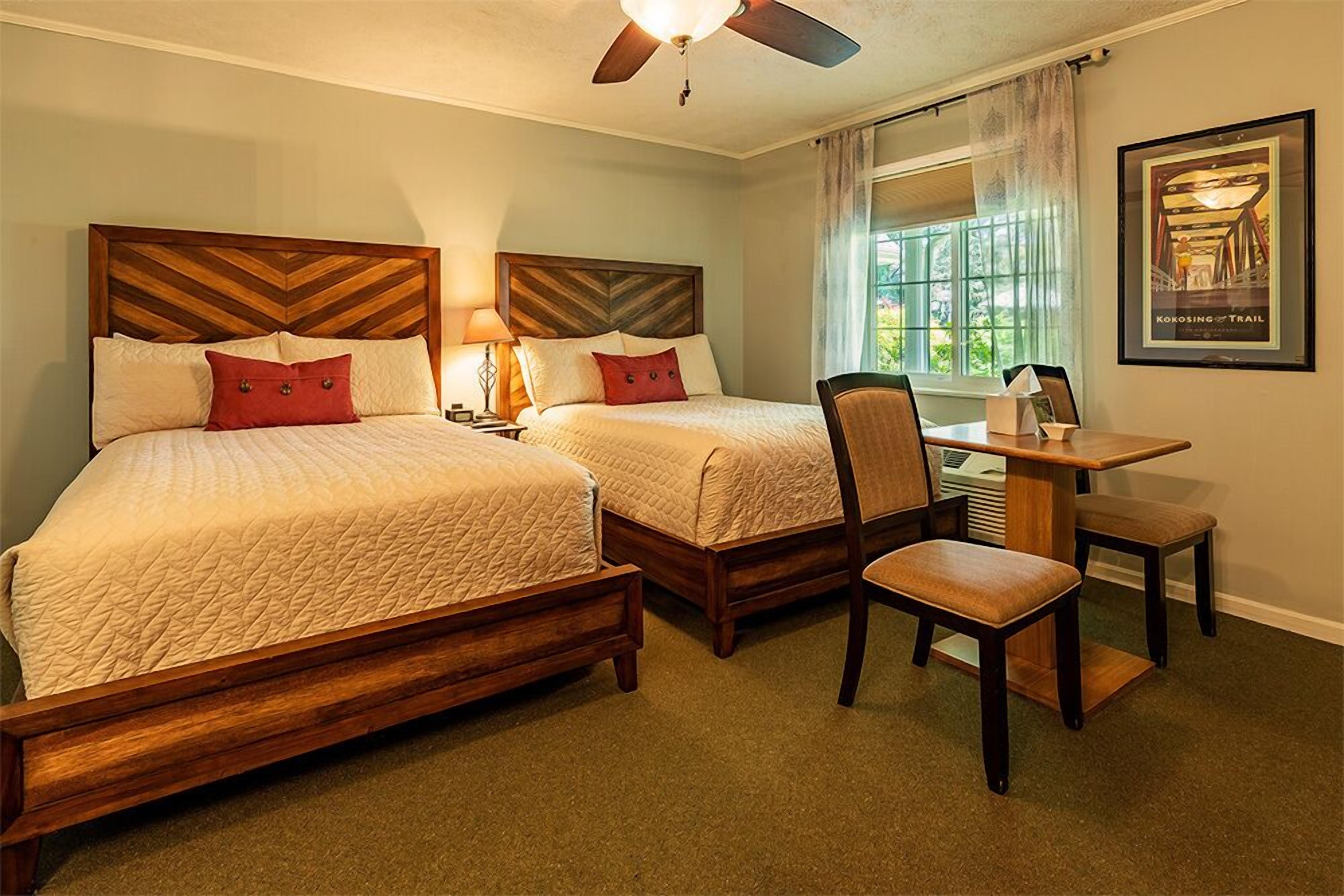 A hotel room with two beds, a desk, and a chair.