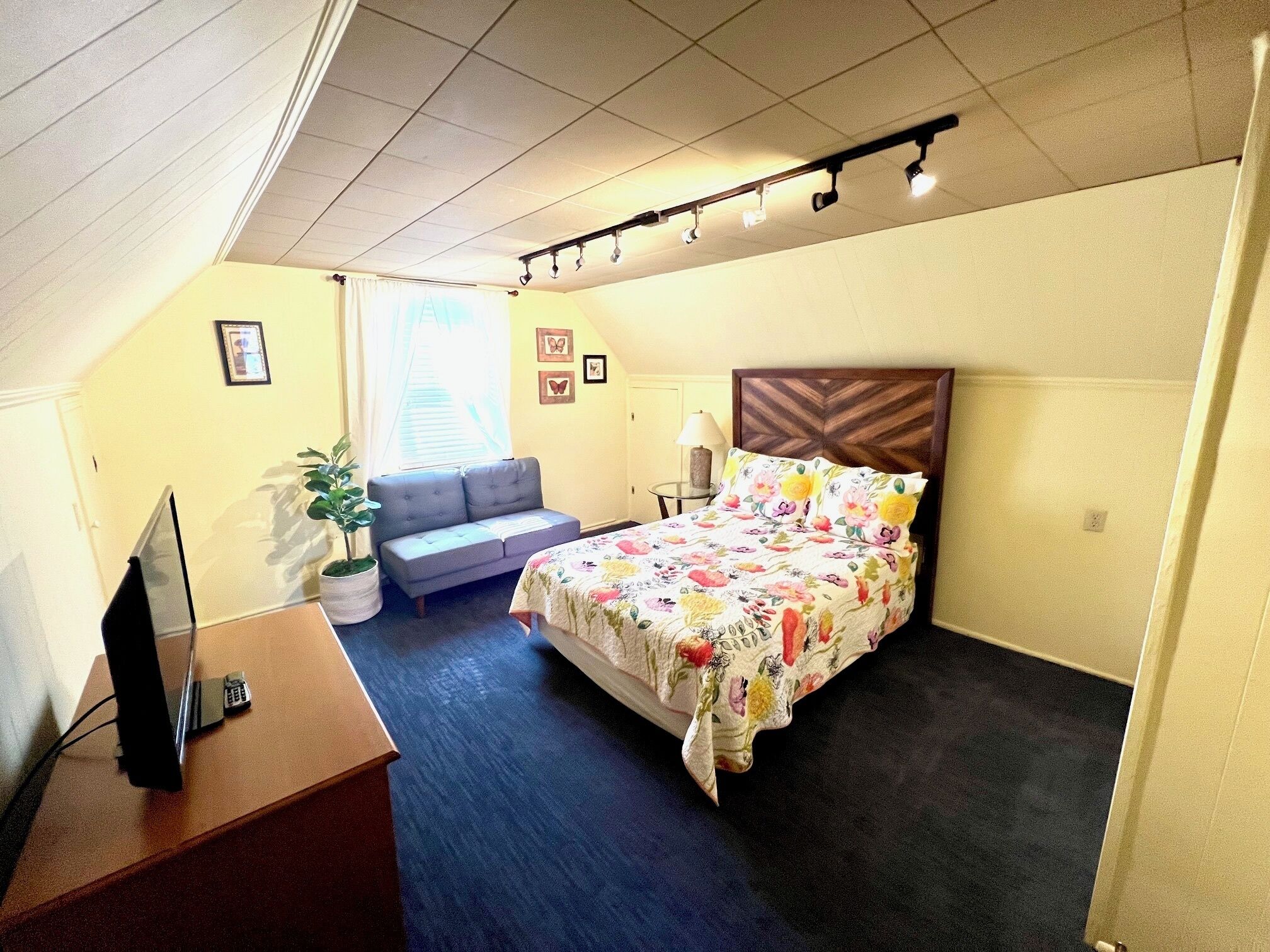 A hotel room with a bed, a sofa, a desk with a computer, a lamp, and a window with curtains.
