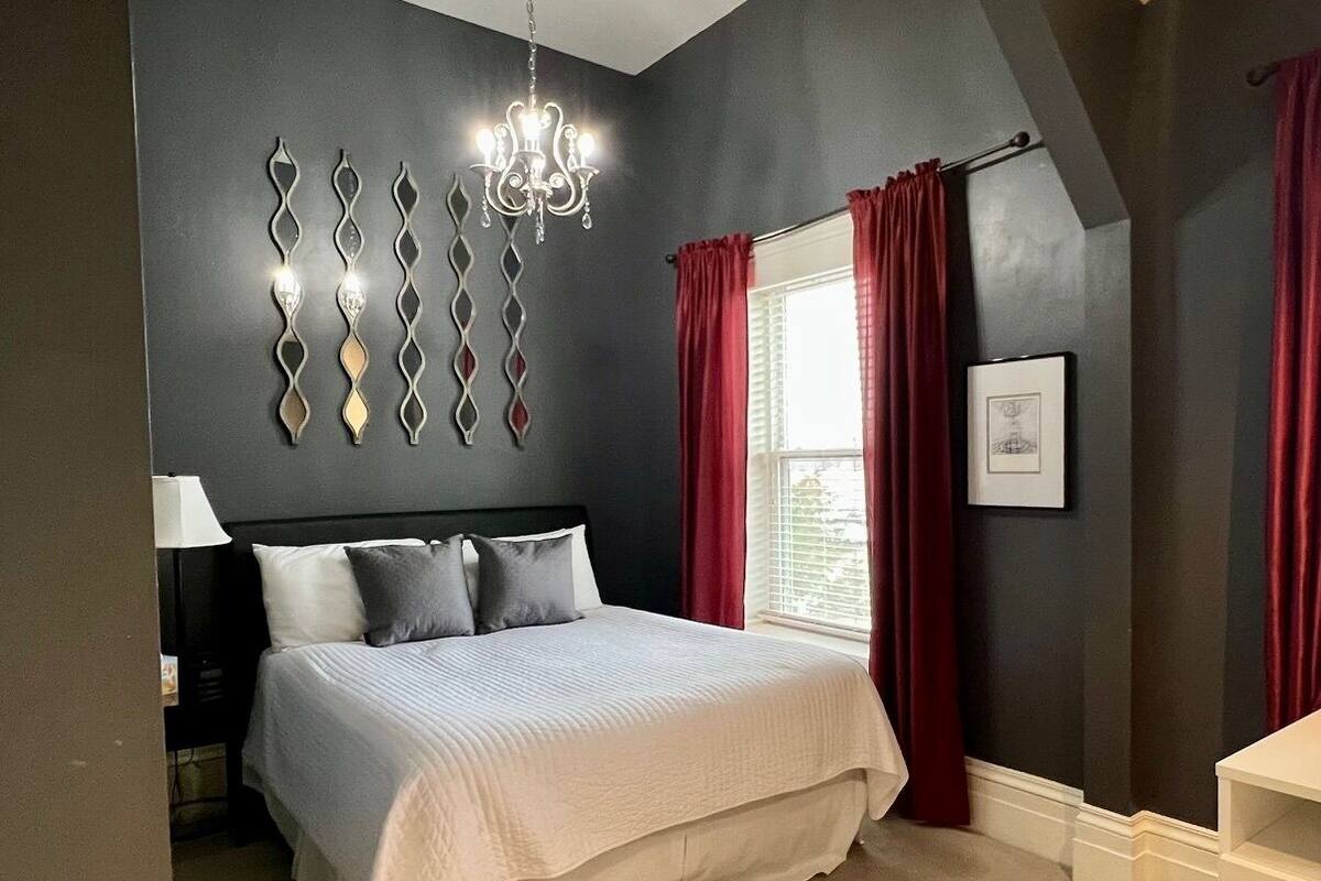 A bedroom with a bed, a chandelier, and a window with curtains.
