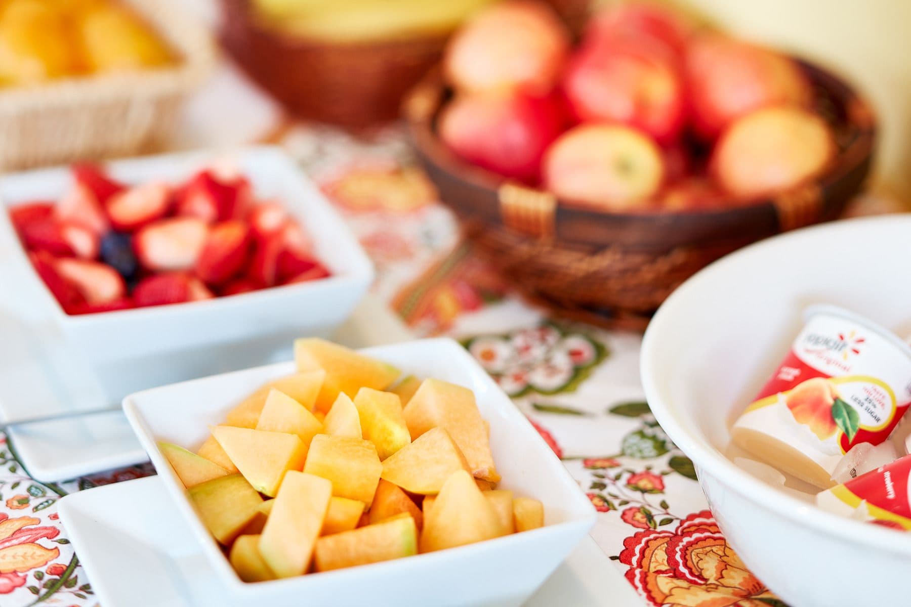 A table with various bowls of fruit and a basket of apples.