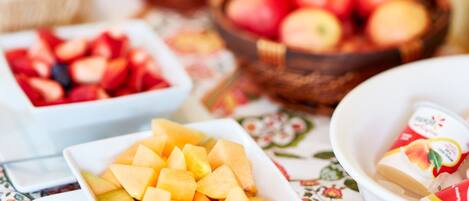 A table with various bowls of fruit and a basket of apples.