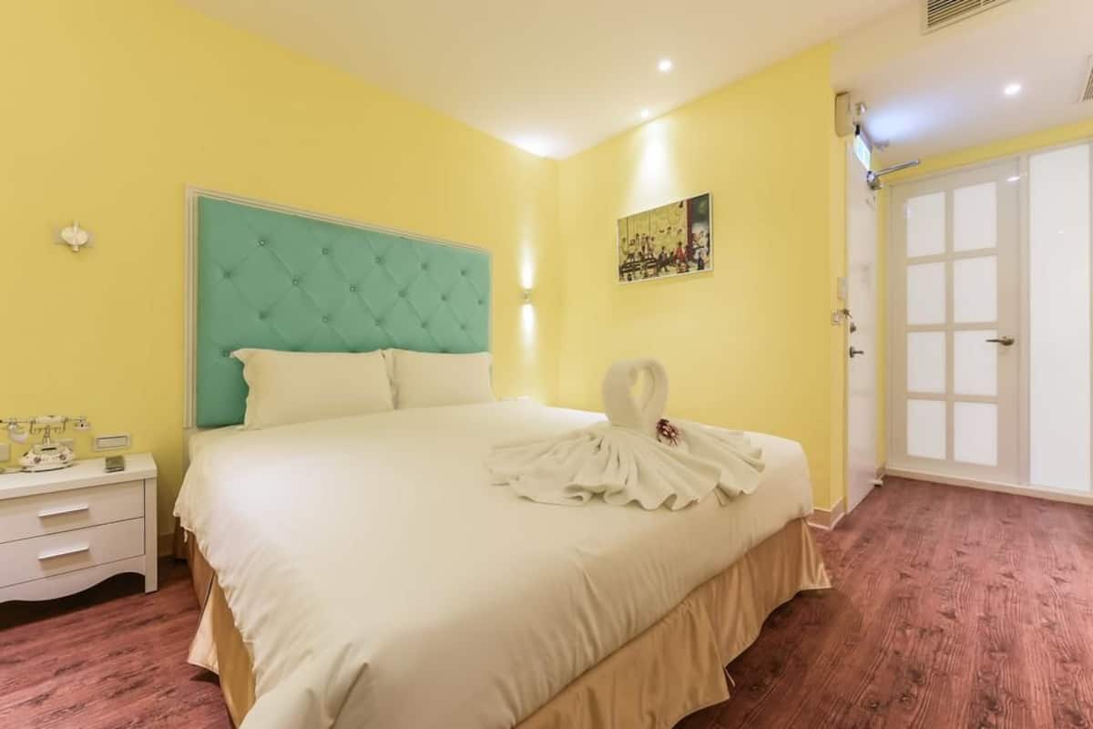 Une chambre d’hôtel avec un grand lit, une table de chevet, une lampe fixée au mur et une porte.