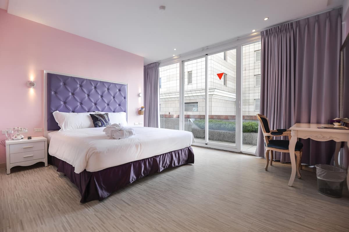 Une chambre avec un grand lit, un bureau et une chaise. Il y a une fenêtre avec des rideaux et une vue sur l’extérieur.