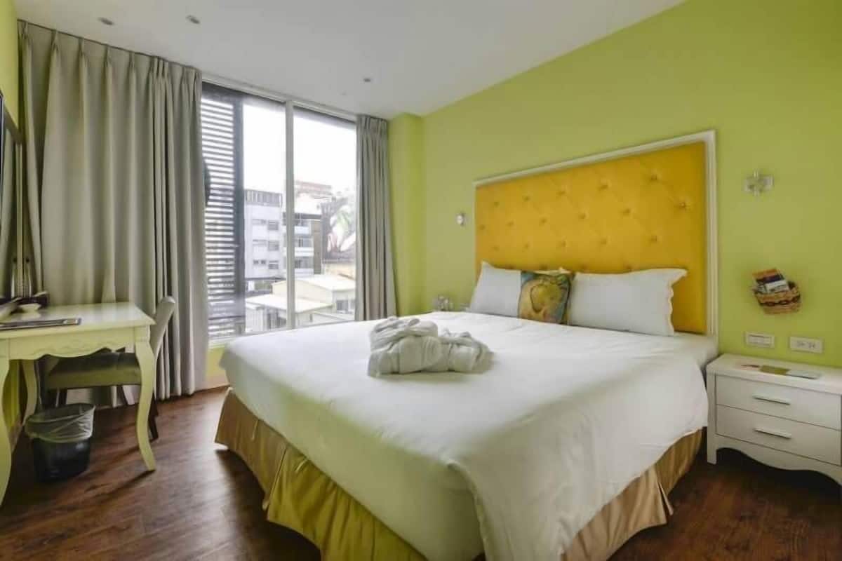 Une chambre d’hôtel avec un grand lit, un bureau et une fenêtre avec des rideaux.