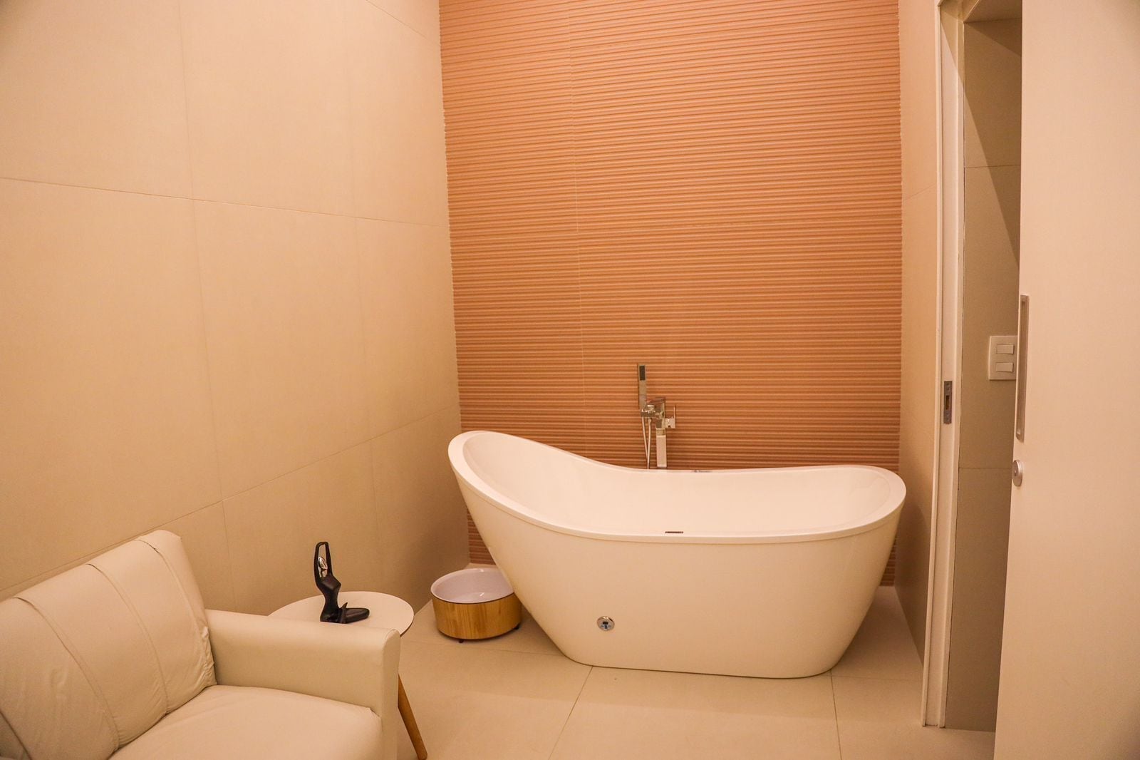 Un baño moderno con una bañera independiente, una pequeña mesa redonda y un objeto decorativo, además de un revestimiento de pared de madera.