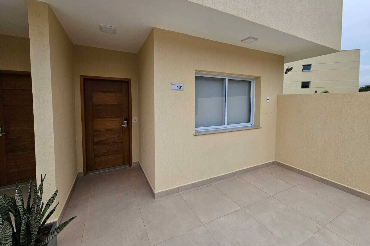Un edificio residencial con fachada color crema, puerta de madera, ventana con letrero de número y suelo de baldosas.