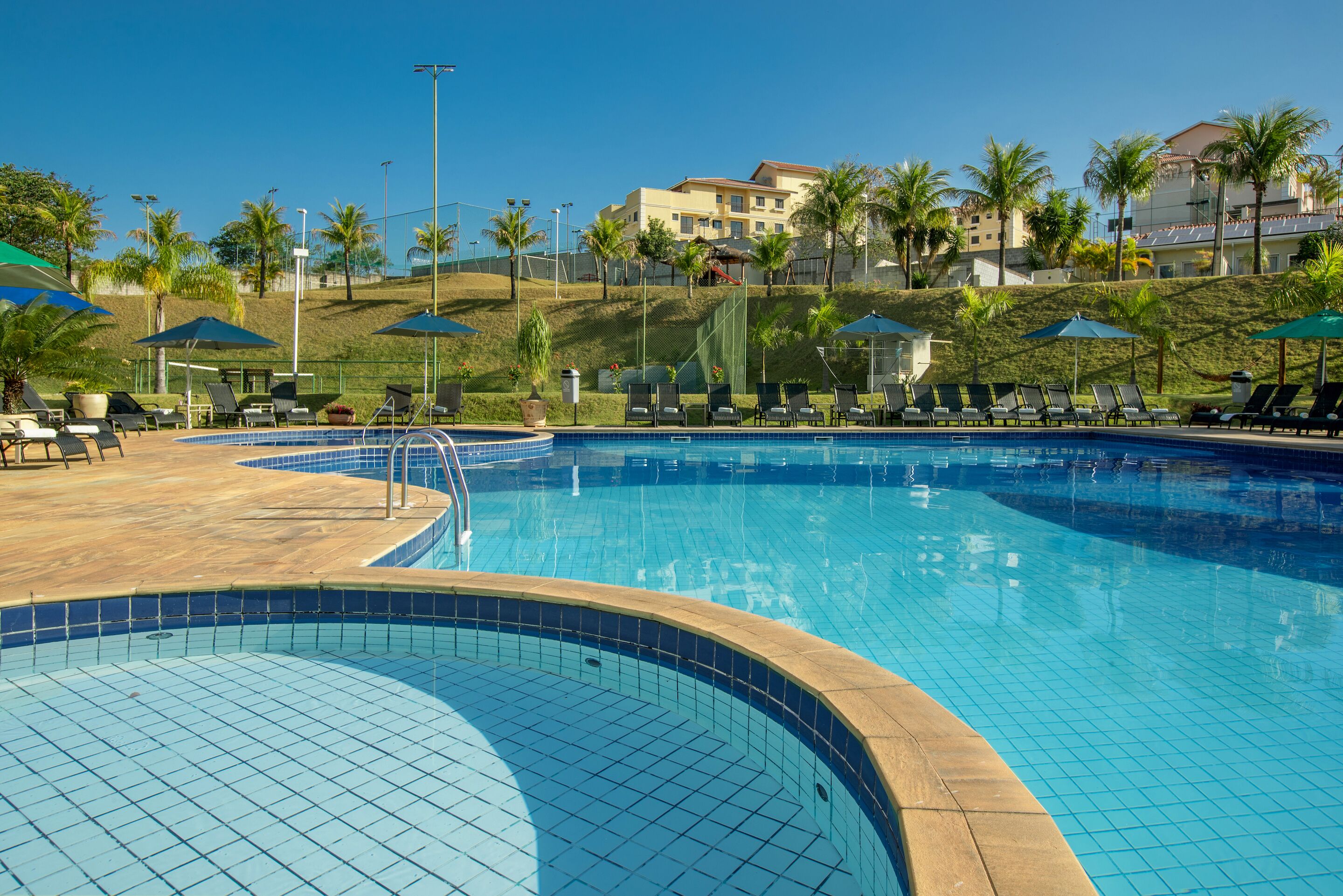 A swimming pool with tiled edges, sun loungers, and umbrellas.