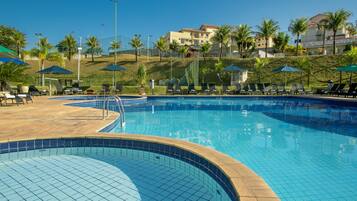 A swimming pool with tiled edges, sun loungers, and umbrellas.