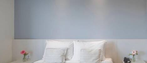 A modern bedroom with a large bed, two bedside tables, and a nightstand with a phone.