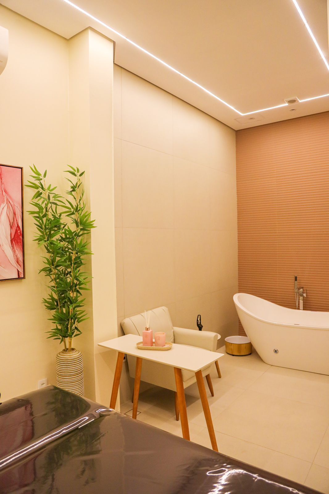A modern bathroom with a freestanding bathtub, a small table with candles, a potted plant, and a large mirror.