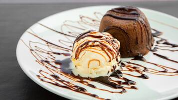 Un plato de postre con una bola de helado de vainilla y un postre de chocolate, rociado con salsa de chocolate.