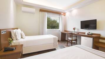 A hotel room with two beds, a desk, a television, and a small refrigerator.